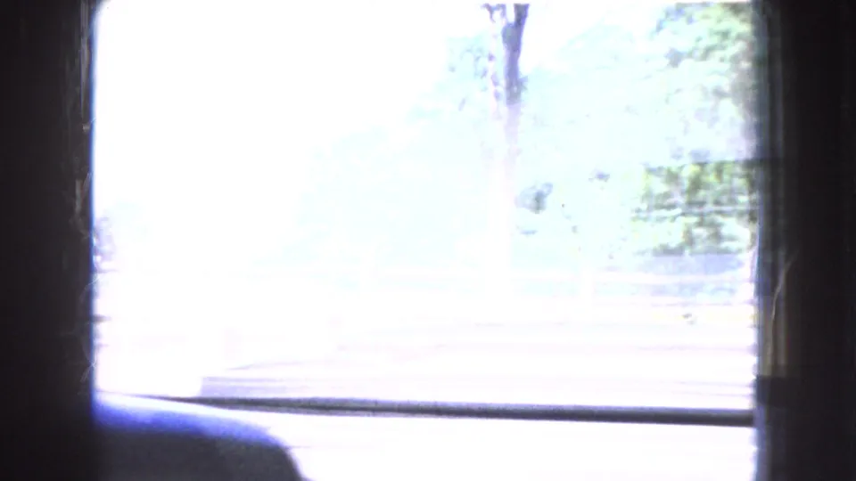1966 Ohio 8mm frame with a bright overexposed roadside or park view beyond dark interior framing, with faint trees and ground visible at the edge.