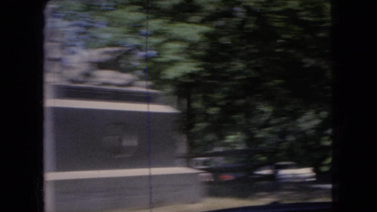 Blurred roadside view with a small structure, trees, and dark car interior framing.