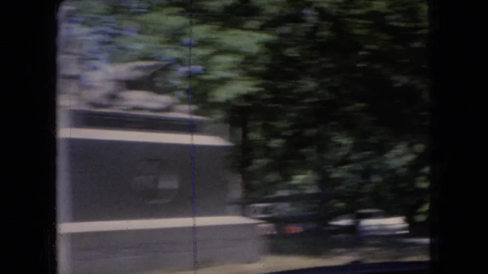 Moving 8mm view from a car in Ohio, 1966, with motion-blurred trees, a small roadside structure, dark window framing, and vertical film wear.