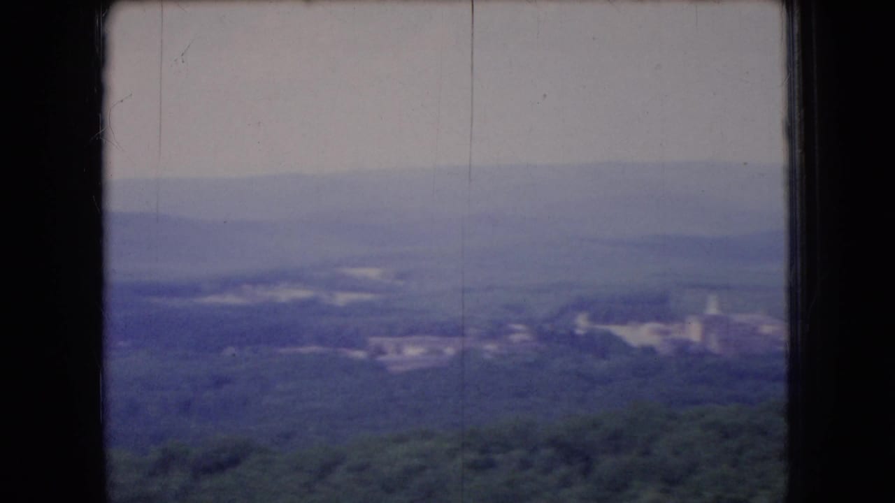 Forested hills and distant ridges seen through a dark window frame.