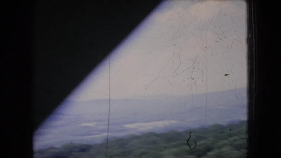 1966 Ohio home-movie frame with forested hills and distant haze partly blocked by a dark diagonal window or frame shadow.