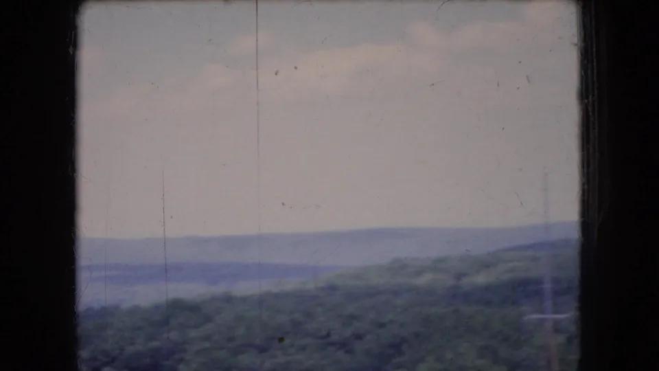 1966 Ohio 8mm frame showing a hazy horizon of wooded hills, muted sky, and dark window framing at the edge.