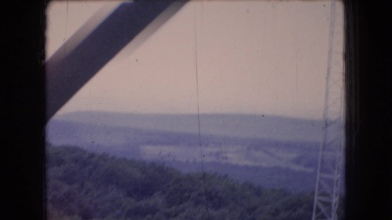 1966 Ohio 8mm view through a dark cabin or window frame toward a hazy forested valley, with cable or tower structure visible near the right edge.