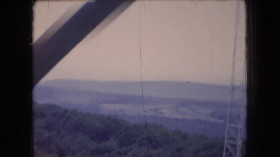 1966 Ohio 8mm view through a dark cabin or window frame toward a hazy forested valley, with cable or tower structure visible near the right edge.