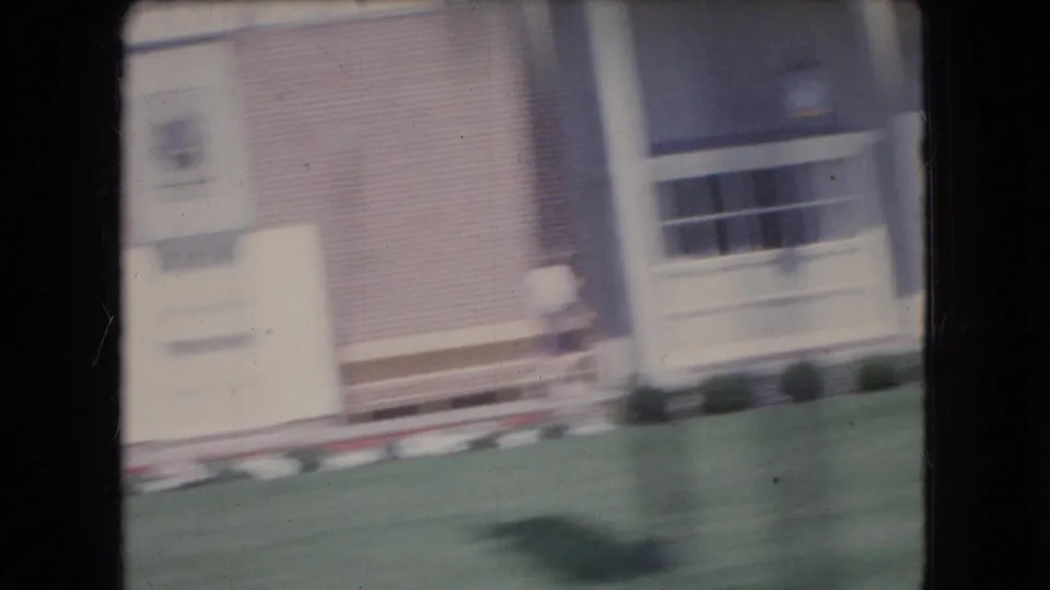 Motion-blurred 1966 Ohio street view showing a brick building, lawn or planted strip, windows, and a sidewalk edge from a moving car.