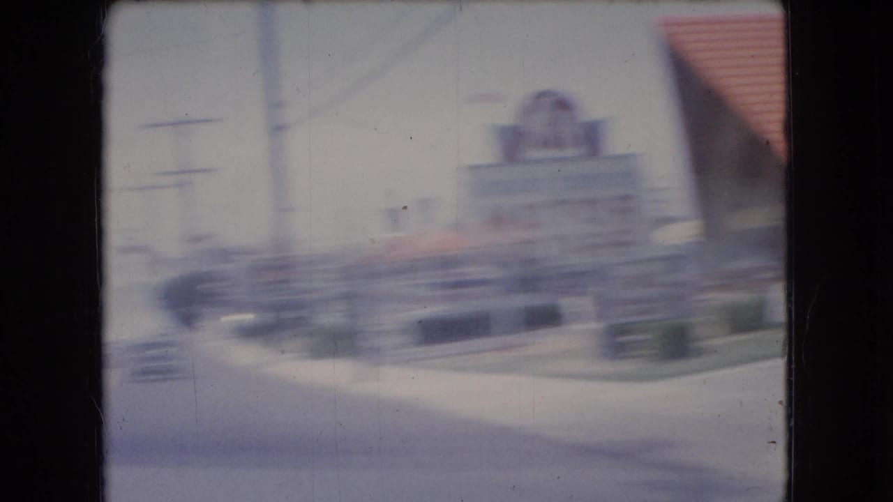 Soft, motion-blurred 1966 home-movie view of roadside buildings and storefront shapes filmed from a moving car in the United States.