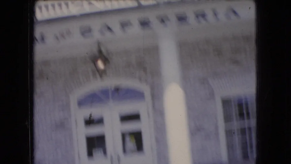 Close, tilted passenger-window view of a brick building facade with an arched entrance, windows, and soft 8mm motion blur.