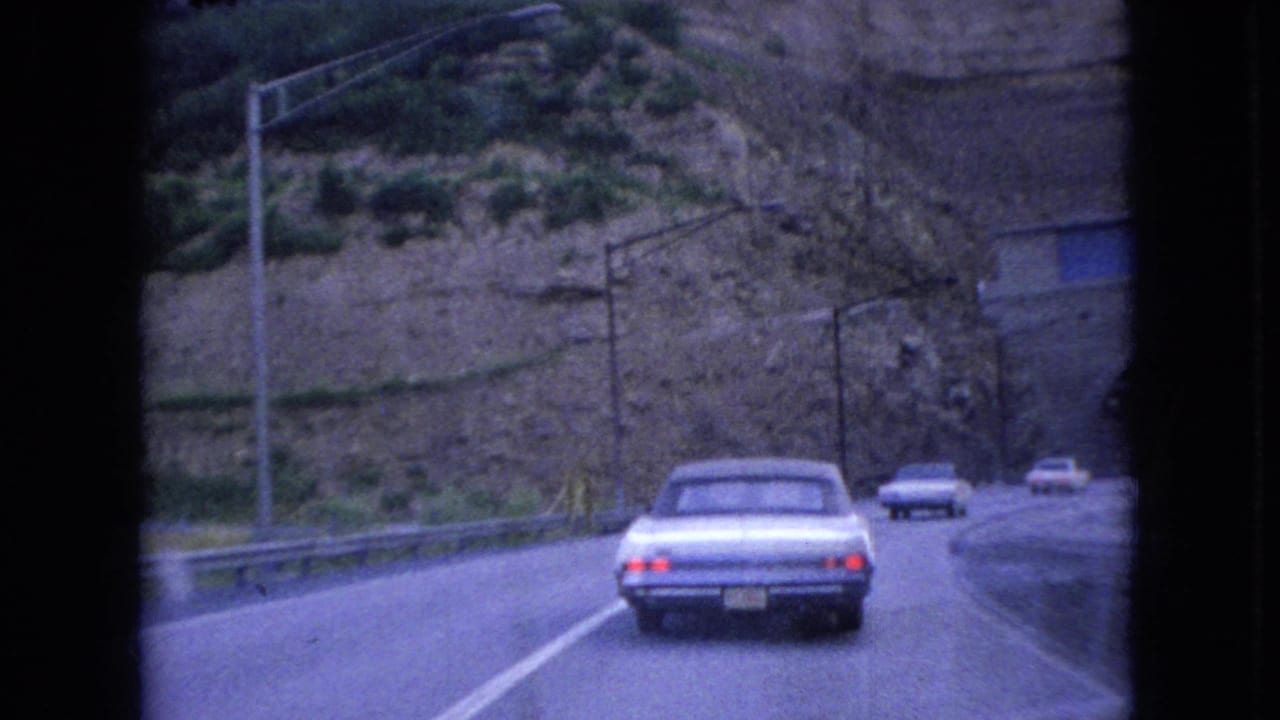 White sedan continuing along the road with other cars ahead near a tunnel area.