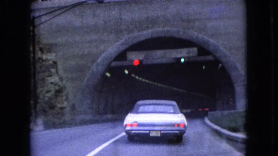 The sedan continues toward the dark tunnel opening, with the stone arch, roadside curb, and overhead signal lights visible in the 1966 Ohio road scene.