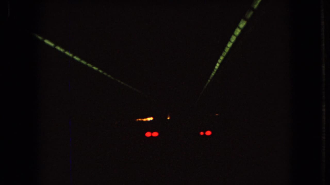1966 Ohio 8mm home-movie frame showing a car from behind in a dark tunnel, with red taillights and converging tunnel lighting.