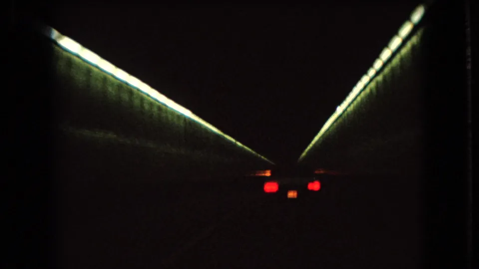 1966 Ohio 8mm frame of a car traveling through a dark tunnel, with greenish linear lights converging toward the roadway ahead.