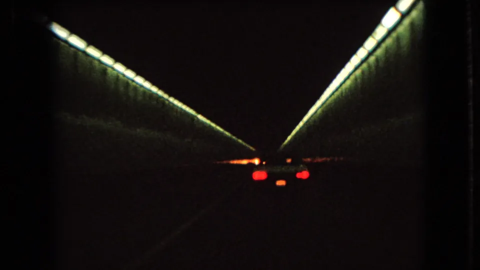 1966 Ohio home-movie frame showing a car deeper inside a dark tunnel, with red taillights below bright fluorescent-style side lighting.