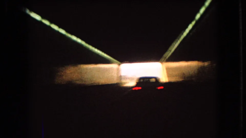 1966 Ohio 8mm frame showing a car nearing the illuminated exit of a dark tunnel, with converging lights and heavy contrast.