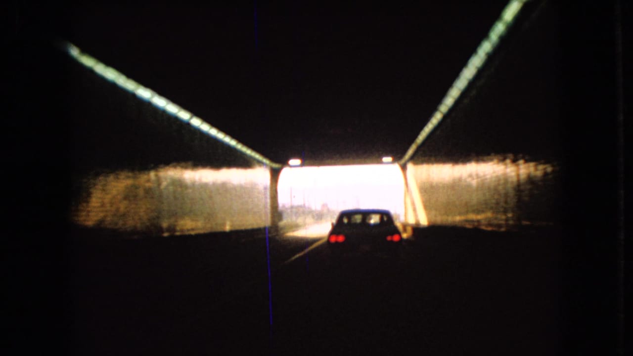 1966 Ohio 8mm frame showing a car viewed from behind inside a dark tunnel, with red taillights and a bright roadway exit ahead.