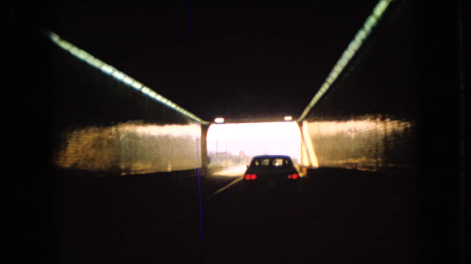1966 Ohio 8mm frame showing a car viewed from behind inside a dark tunnel, with red taillights and a bright roadway exit ahead.