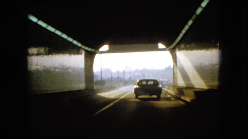1966 Ohio home-movie frame of a car moving through a tunnel toward daylight, with pale concrete walls and overhead lights visible.
