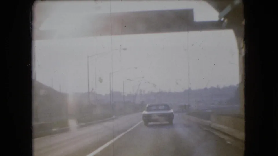 1966 Ohio 8mm frame showing the car outside or near the tunnel exit on a hazy roadway, with poles and roadside barriers visible.