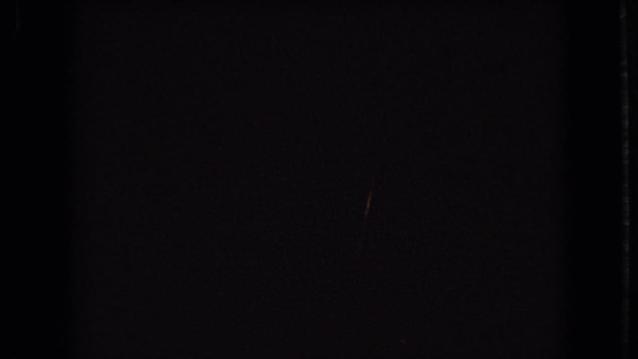 A dark 8mm contact-frame view shows only a partial lower strip of a 1966 Ohio house under construction, with pale sheathing and trees just visible.