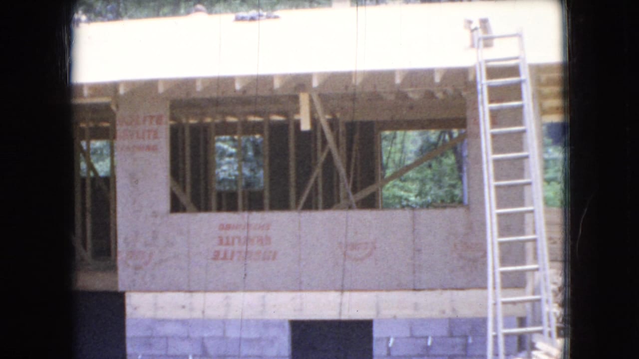 House under construction with open window bays, exterior sheathing, and a ladder leaning at the right.