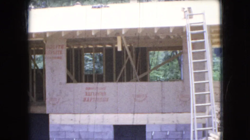 A 1966 Ohio residential construction scene shows exposed framing, wall sheathing with red stenciled markings, open window bays, and a tall ladder leaning against the right side.