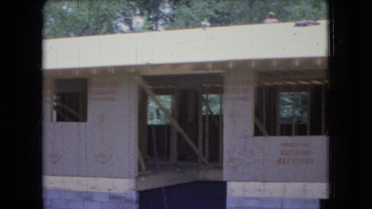 1966 Ohio 8mm frame showing a country home under construction with exposed wooden framing, protective sheathing, and trees behind the roofline.