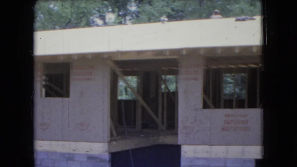 1966 Ohio 8mm frame showing a country home under construction with exposed wooden framing, protective sheathing, and trees behind the roofline.