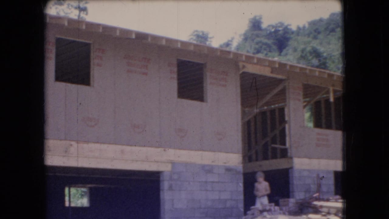1966 Ohio 8mm frame showing a house under construction near trees, with exterior sheathing, concrete block foundation, open wall sections, scattered lumber, and a worker in light clothing.