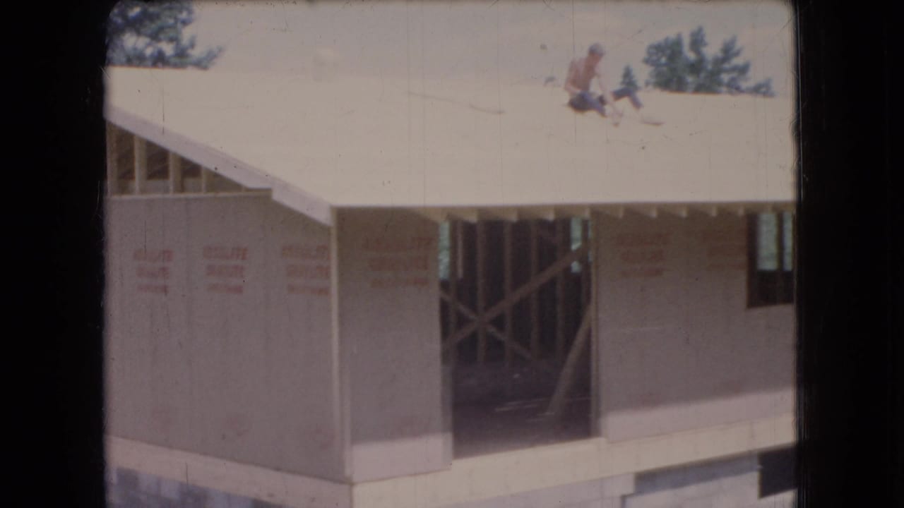 1966 Ohio 8mm frame showing a new garage under construction with sheathing installed, exposed roof framing, and workers visible on the roof.