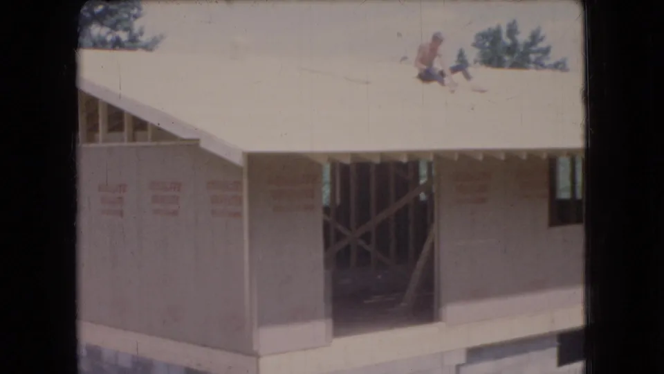 1966 Ohio 8mm frame showing a new garage under construction with sheathing installed, exposed roof framing, and workers visible on the roof.