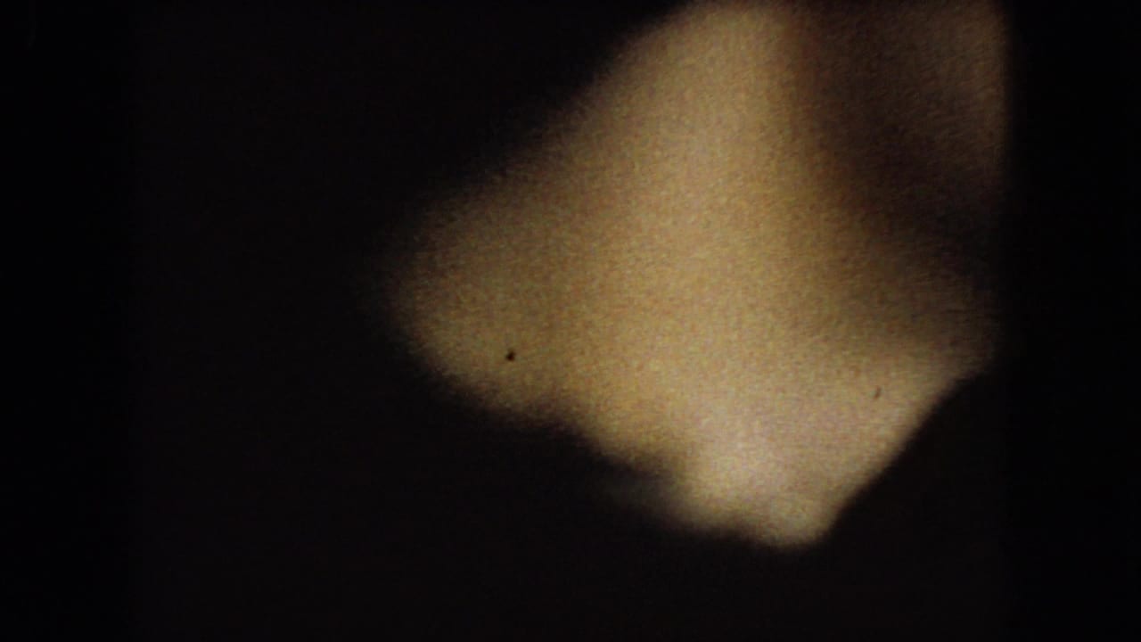 Low-light 8mm frame from the supplied 1966 Ohio clip showing a dark car interior, a blurred foreground figure, and a partially visible window during rainy travel.