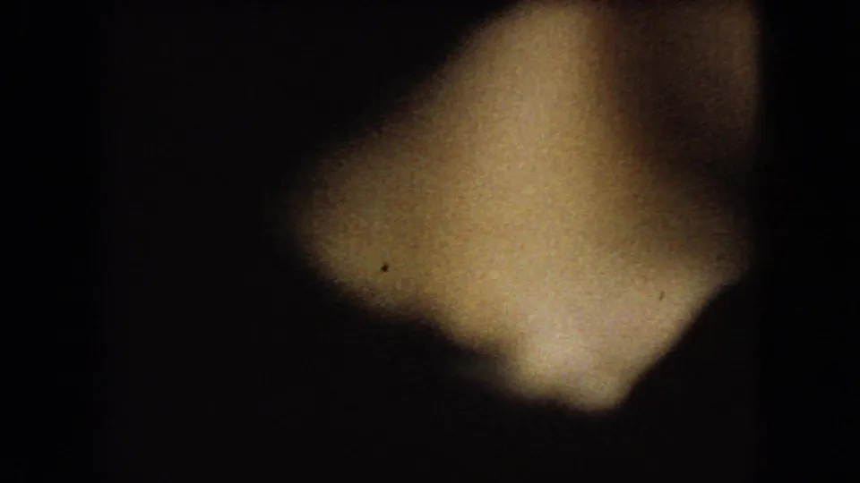 Low-light 8mm frame from the supplied 1966 Ohio clip showing a dark car interior, a blurred foreground figure, and a partially visible window during rainy travel.