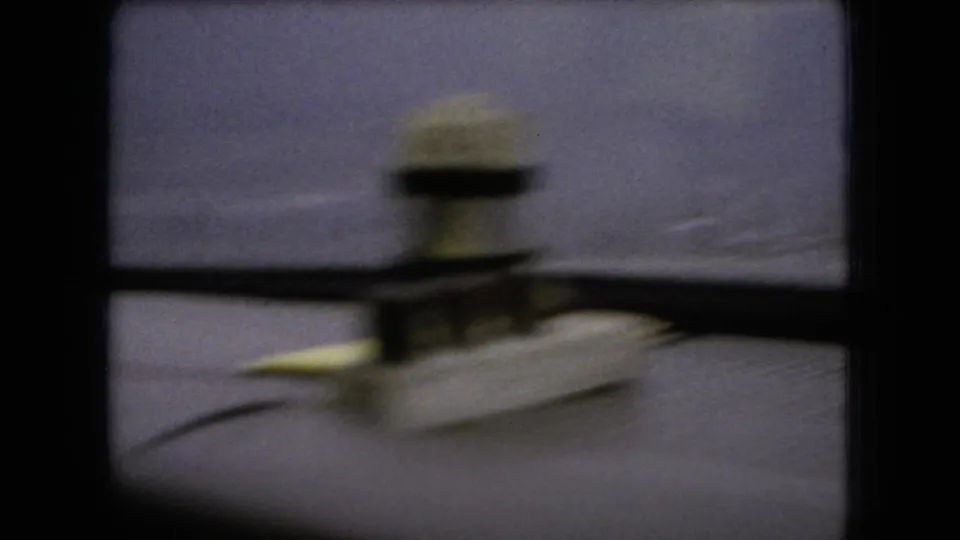 1966 Ohio 8mm frame showing a blurred dashboard or windshield-mounted object inside the car, with the wet roadside view fading into a purple-blue cast beyond.