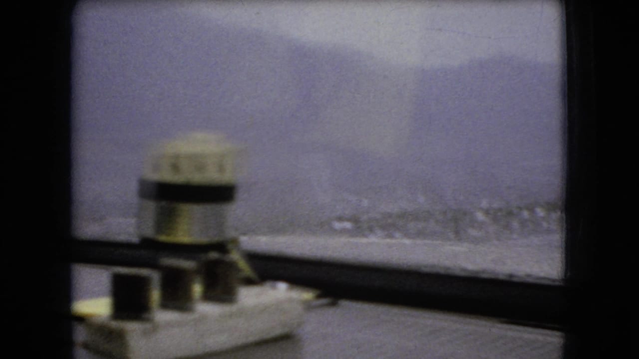 1966 Ohio 8mm home-movie frame from inside a moving car, showing a divided windshield, cloudy sky, distant rural land, and a small object on the dashboard.