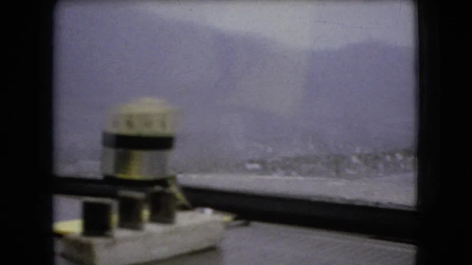 1966 Ohio 8mm home-movie frame from inside a moving car, showing a divided windshield, cloudy sky, distant rural land, and a small object on the dashboard.