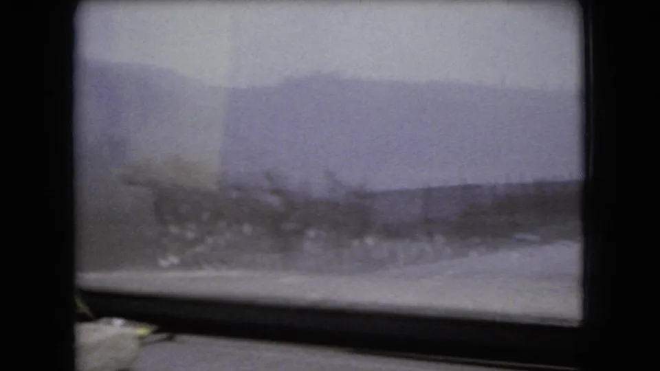 1966 Ohio 8mm frame showing a hazy rural horizon, pale cloudy sky, windshield frame, and blurred roadside vegetation from an interior vehicle perspective.