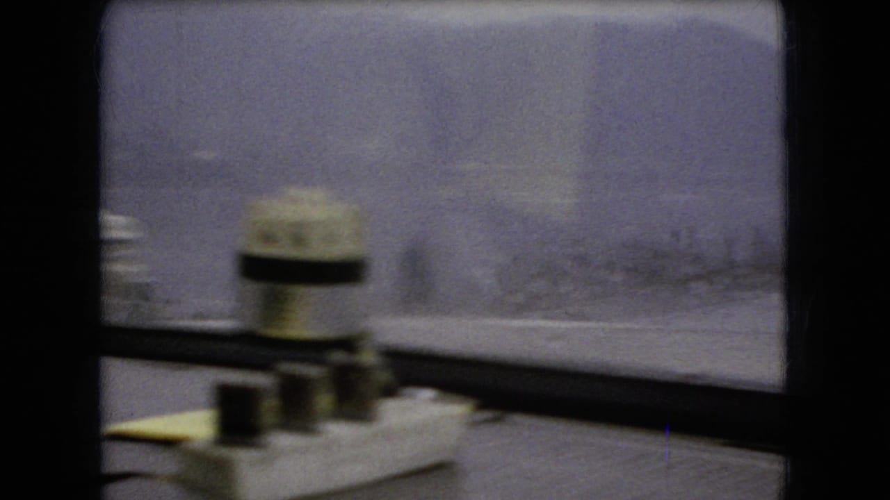 1966 Ohio 8mm frame from inside a car, showing rain-blurred windows, dashboard objects, and an overcast roadside landscape outside.