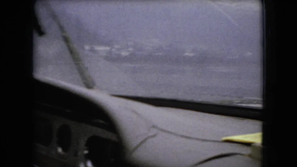 1966 Ohio home-movie view through a rain-streaked windshield, with wet pavement, blurred roadside detail, and traffic movement ahead.