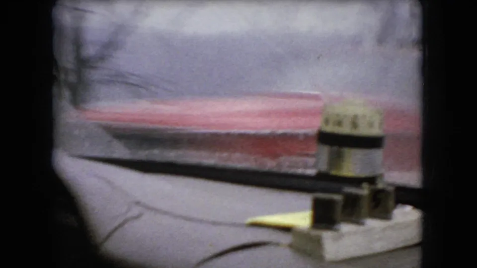 1966 Ohio 8mm frame showing a red vehicle passing beyond wet car glass, with interior dashboard details and overcast road conditions visible.