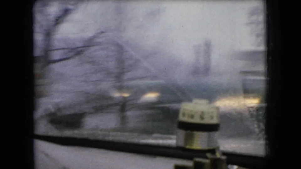 1966 Ohio 8mm home-movie frame showing a wet windshield view from inside a moving vehicle, with blurred roadway and a small cylindrical device on the dashboard.