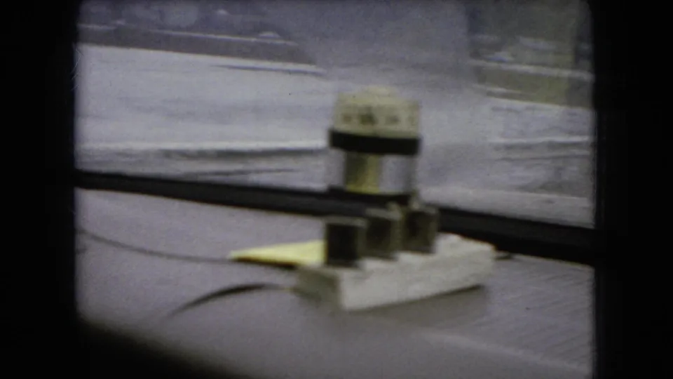 1966 Ohio home-movie frame showing a rain-blurred bridge or road edge through the windshield, with the dashboard device and vehicle interior framing prominent.