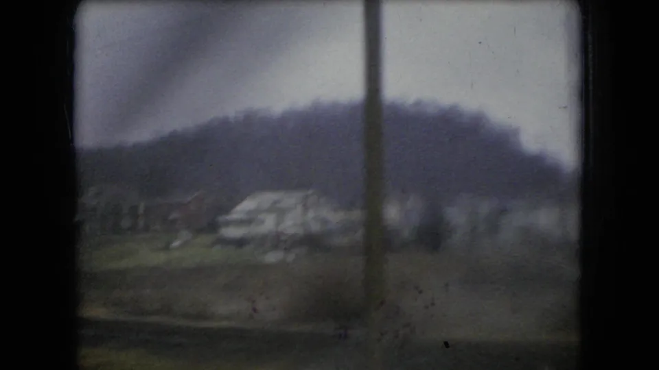 1966 Ohio 8mm frame showing a soft, rain-muted view through a car window toward a wooded hill and indistinct roadside terrain beyond the glass.