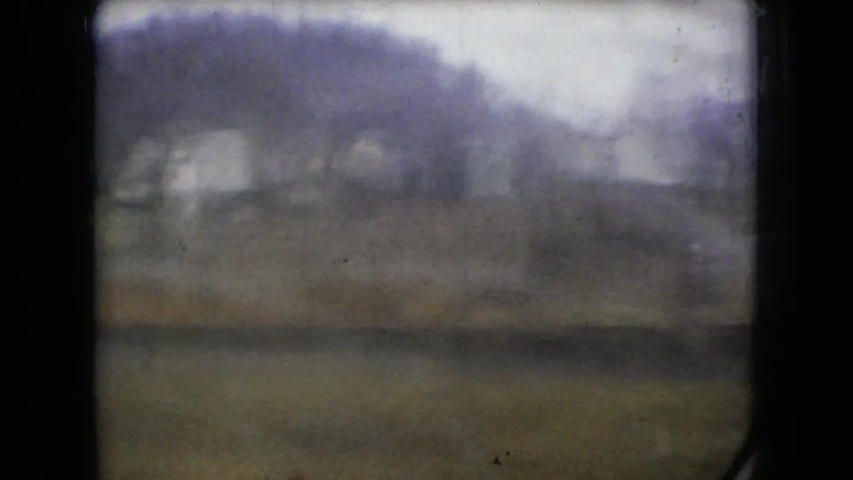1966 Ohio 8mm frame with a heavily softened rainy car-window view of low wooded hills, muted roadside ground, and overcast light.