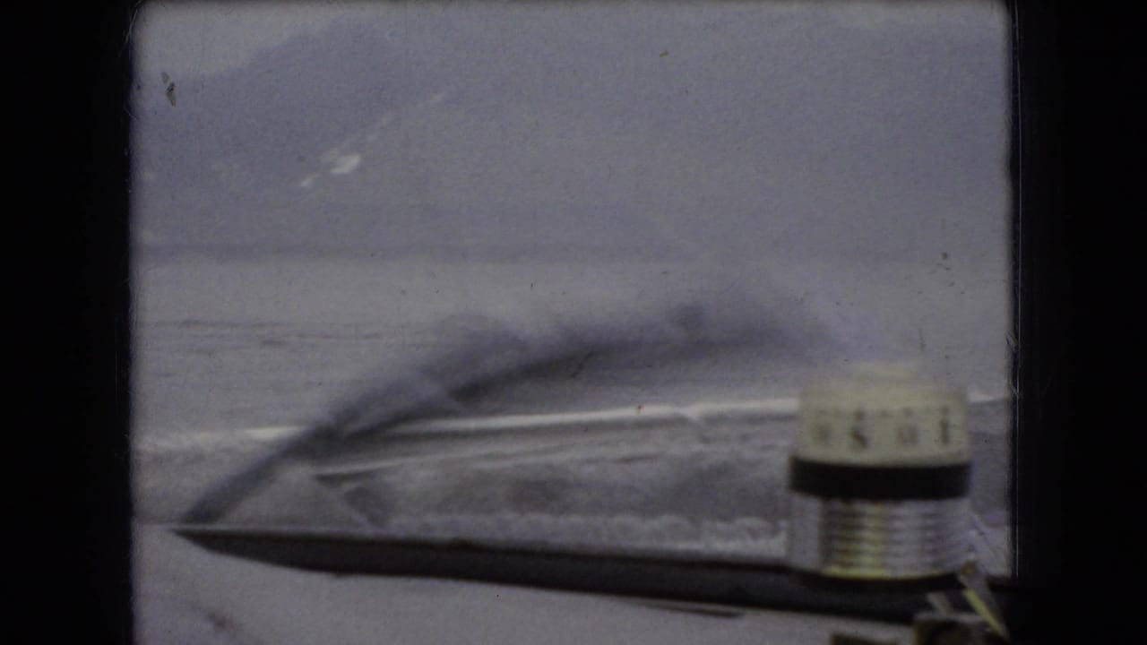 1966 8mm home-movie frame from supplied Ohio metadata, looking through a car windshield toward a gray water horizon with the wiper and hood visible.
