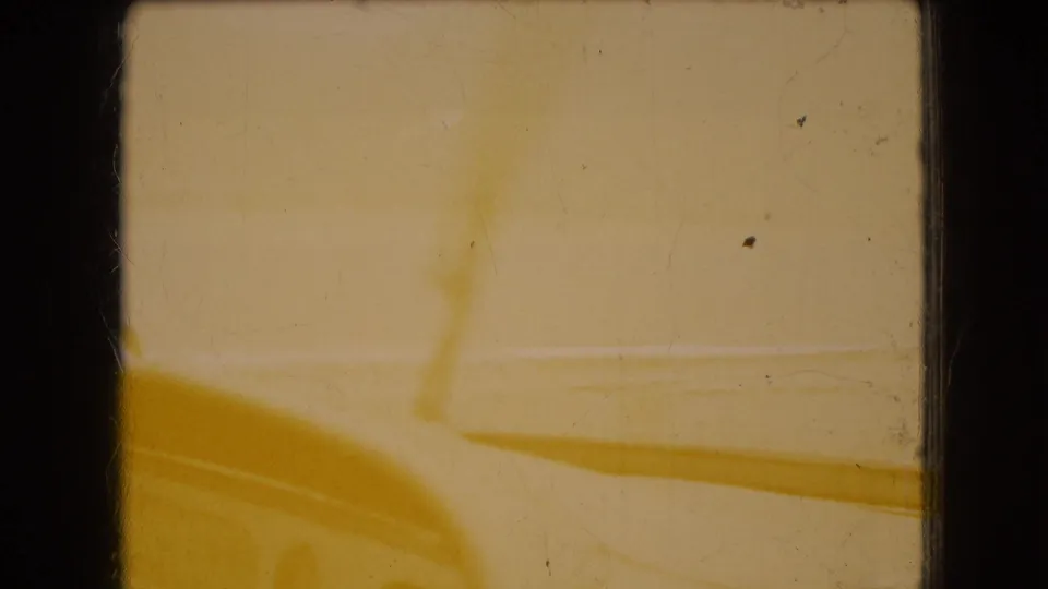 Color-shifted 8mm frame with a yellow cast, faintly showing the car hood, windshield wiper, and horizontal waterline through the windshield.