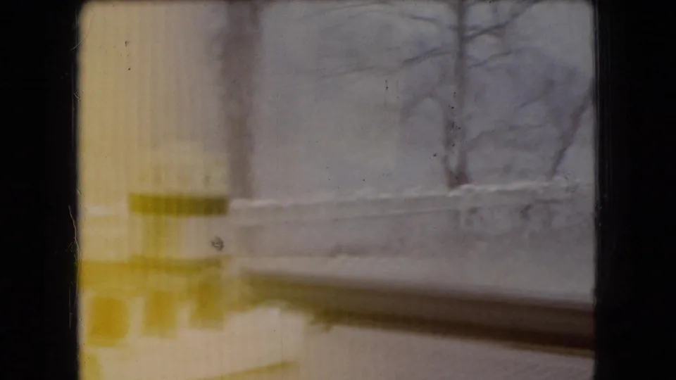 1966 Ohio 8mm home-movie frame showing a blurred roadside or bridge edge, bare tree forms, and weather-softened motion through yellow-tinted film.