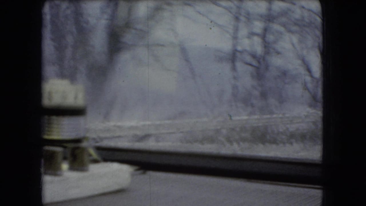 Windshield view of a winter roadside with bare trees, snow, and a small object on the dashboard.