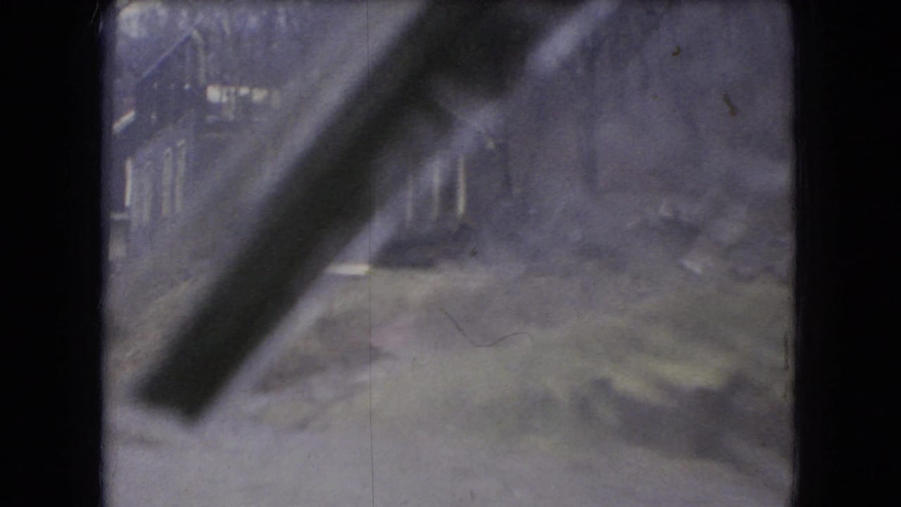 Rain-streaked 8mm view from a moving vehicle in Ohio, 1966, with soft outlines of houses, bare trees, and a road edge beyond the windshield.