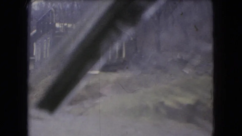 Rain-streaked 8mm view from a moving vehicle in Ohio, 1966, with soft outlines of houses, bare trees, and a road edge beyond the windshield.