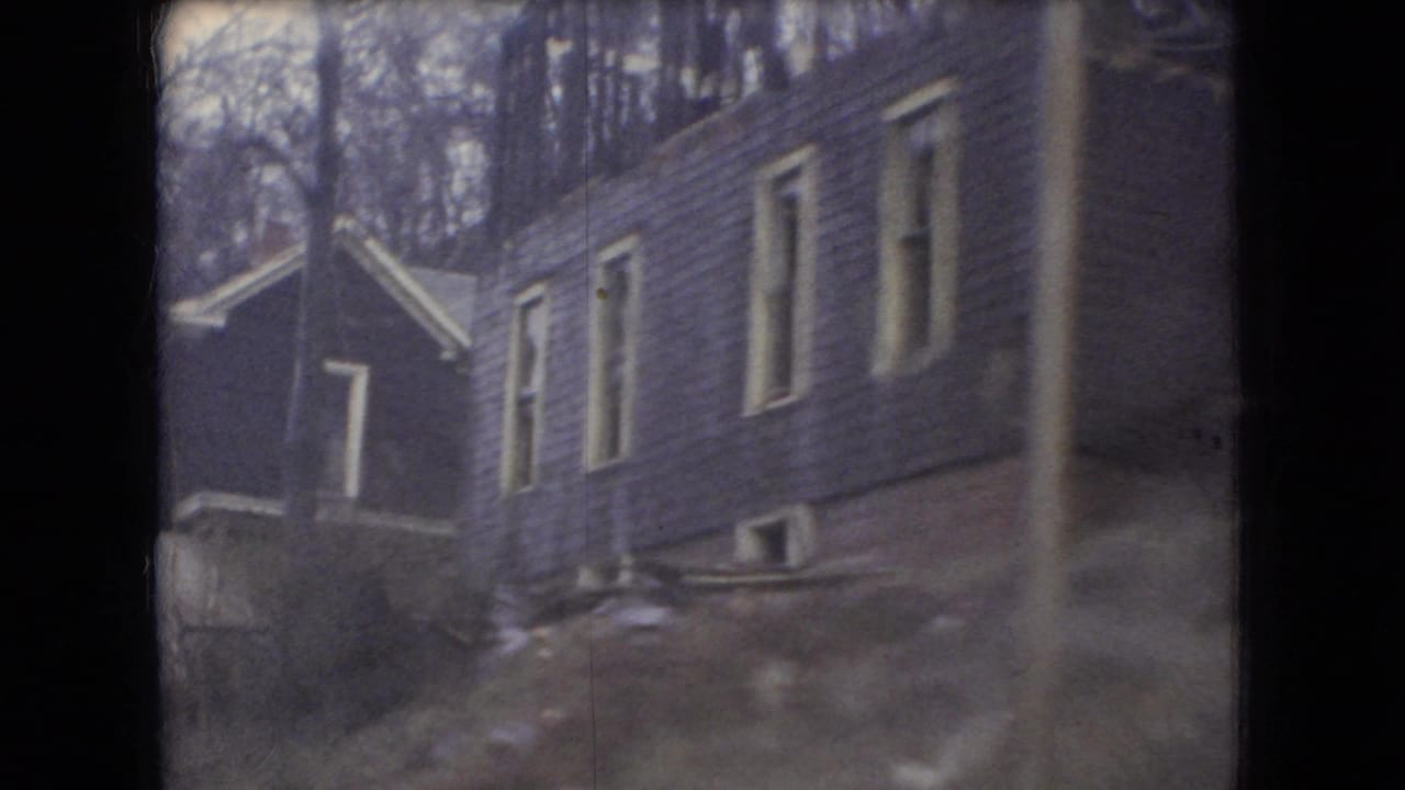 Wood-sided houses on a slope seen from a rainy moving vehicle.