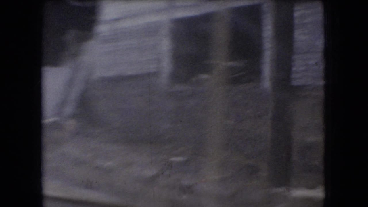 Soft, motion-blurred 8mm view of a weathered roadside wooden building in Ohio, filmed from a moving vehicle in the 1960s.